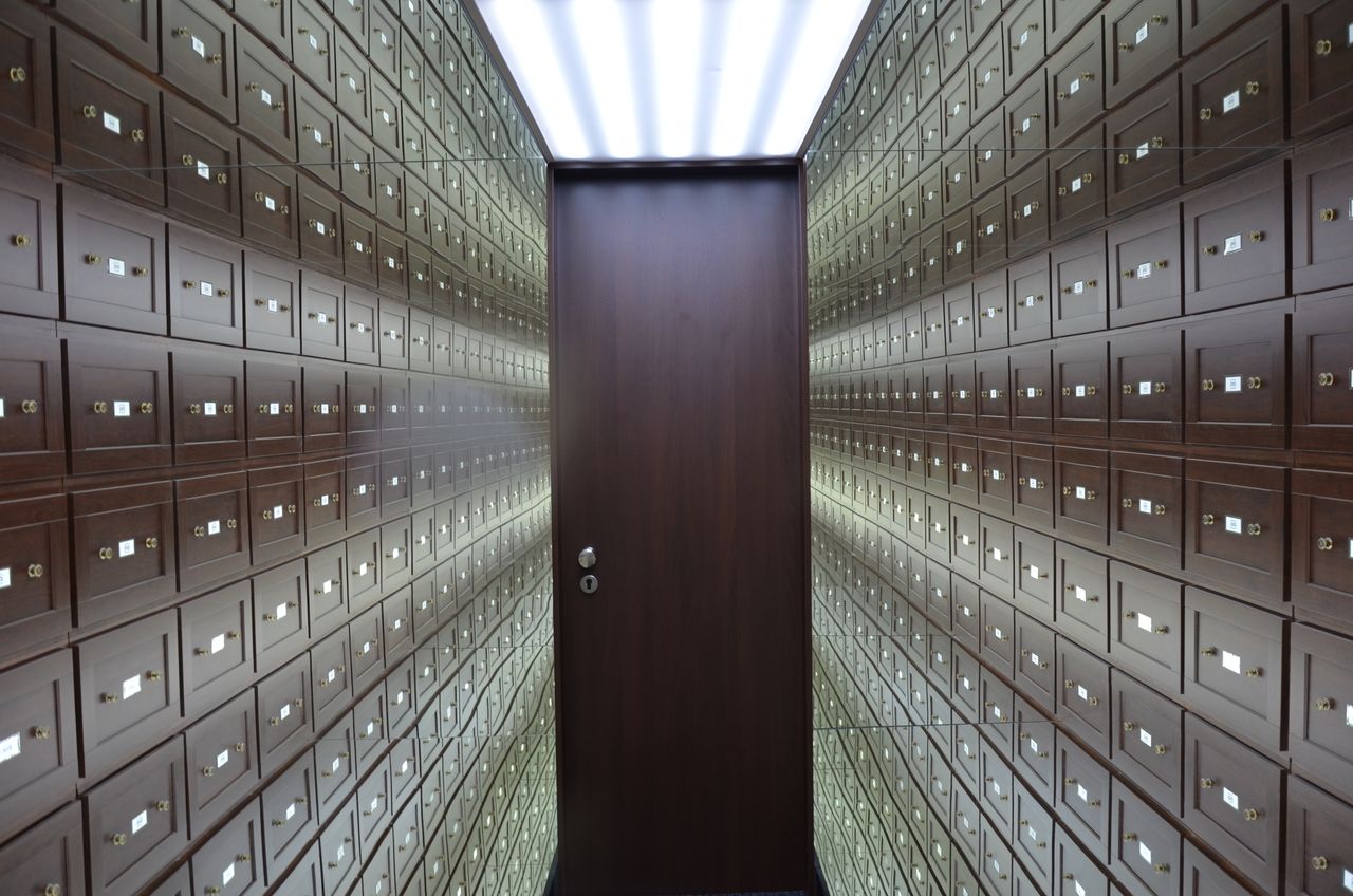 about-img Wooden lockboxes line the walls of a modern, secure vault with a central wooden door.