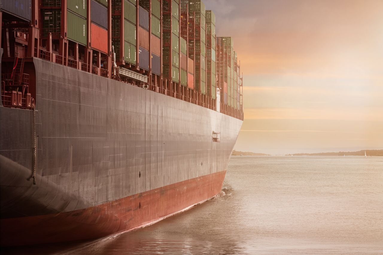 Mastering the First Impression: Your intriguing post title goes here A colossal cargo ship loaded with containers navigates through calm waters against a vibrant sunset sky.